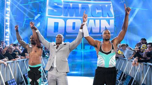 Superluchas - Un grupo de luchadores está parado en un escenario con las manos en alto, con Tyson Kidd.