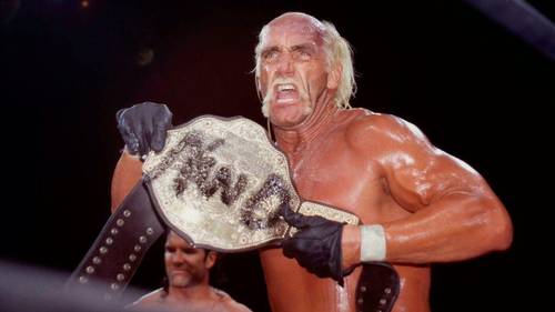 Superluchas - Hulk Hogan sosteniendo un cinturón de lucha libre frente a un ring de lucha libre.