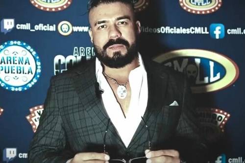 Superluchas - Andrade el Ídolo, también conocido como “La Sombra”, regresa a la Arena México vestido de traje, de pie frente a un fondo azul.
