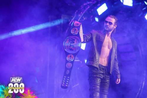 Un hombre sujetando un cinturón de lucha en el escenario, CM Punk también.