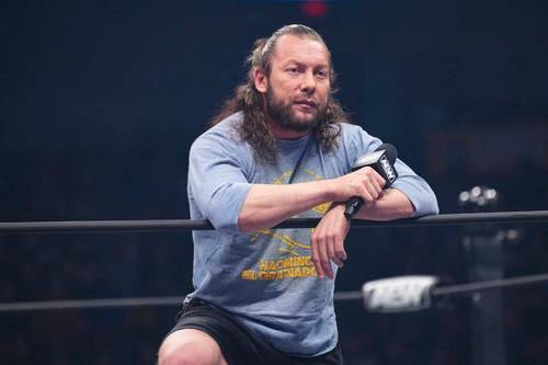 Superluchas - Un hombre de pelo largo sentado sobre una cuerda en un ring de lucha libre mientras Tony Khan ofrece novedades sobre la salud de Kenny Omega.