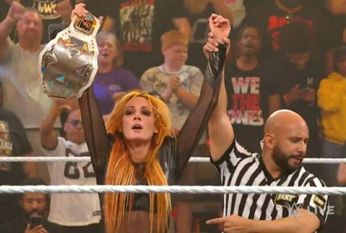 Becky Lynch triunfa como la nueva Campeona de NXT, sosteniendo el cinturón de la WWE frente a un árbitro.