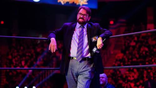 Superluchas - Tony Schiavone observa a un hombre con traje y corbata parado con confianza en un ring de lucha libre, mostrando su amplia experiencia.