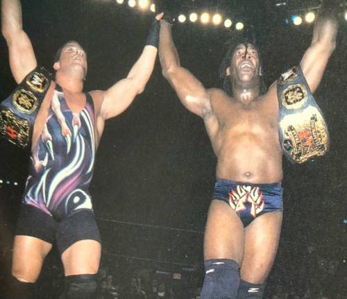 Superluchas - Dos luchadores exhibiendo sus cinturones frente a una multitud durante un campeonato de lucha libre.