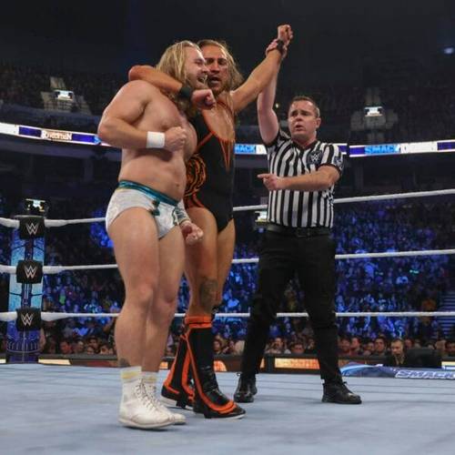 Superluchas - Dos luchadores, Tyler Bate y Superestrella, luchando en un ring de lucha libre con un árbitro durante SmackDown.