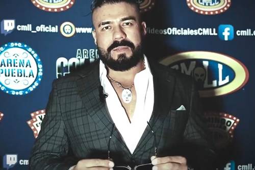 Superluchas - Andrade el Ídolo, también conocido como “La Sombra”, regresa a la Arena México vestido de traje, de pie frente a un fondo azul.