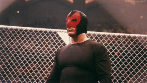 Superluchas - El Escorpión Negro con una máscara roja frente a una valla.