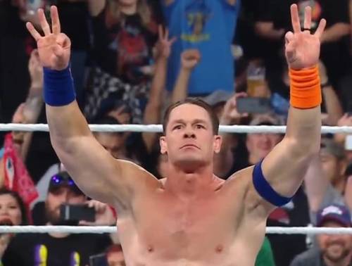 Superluchas - John Cena levanta las manos en el aire durante un evento de la WWE, mostrando su dominio mientras la multitud ruge de emoción.