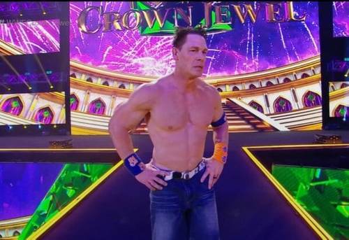 Superluchas - John Cena, un luchador, está de pie en un escenario con un letrero con la joya de la corona al fondo.