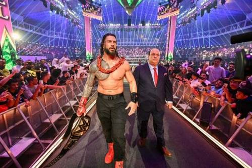Superluchas - Booker T defiende la agenda de Roman Reigns mientras camina con confianza por un escenario frente a una multitud hipnotizada.