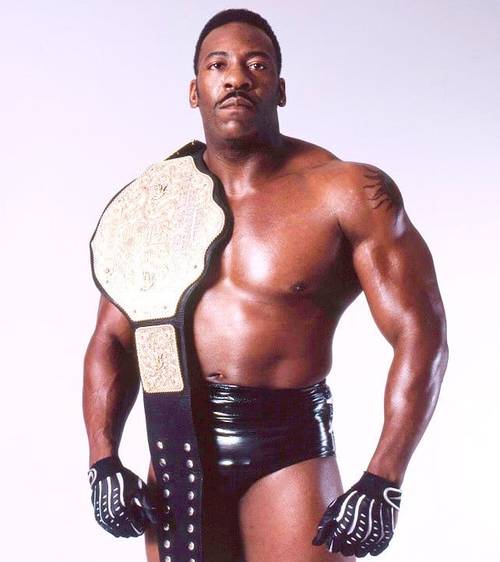Superluchas - Booker T, un luchador con un cinturón, posa frente a un fondo blanco.