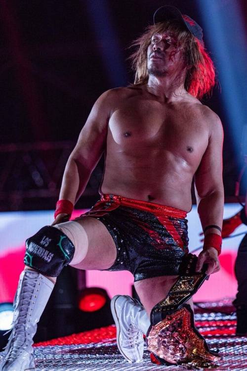 Superluchas - Hiroshi Tanahashi, un luchador, está de pie en un escenario sosteniendo un cinturón.