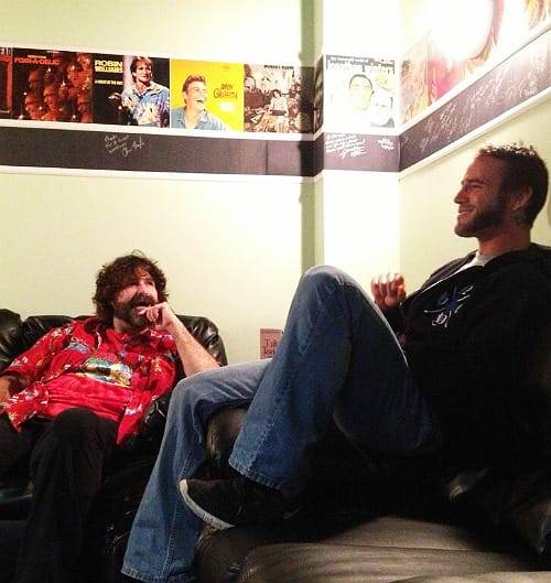 Superluchas - Dos hombres, CM Punk y Mick Foley, están sentados en un sofá hablando entre ellos.