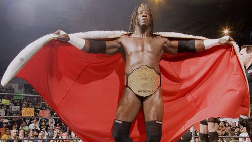 Superluchas - Booker T, un luchador con capa roja, se para cautivadoramente frente a una multitud durante una escena de película.