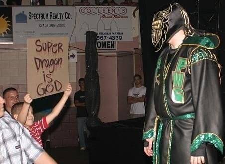 Superluchas - Un hombre vestido de verde se para frente a una multitud en el tradicional fortín de PWG.