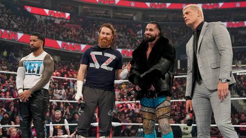 Superluchas - Tres luchadores, incluidos Sami Zayn y Drew McIntyre, parados hombro con hombro en un ring.