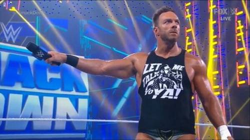 Un hombre está frente a un ring de la WWE sosteniendo un micrófono.