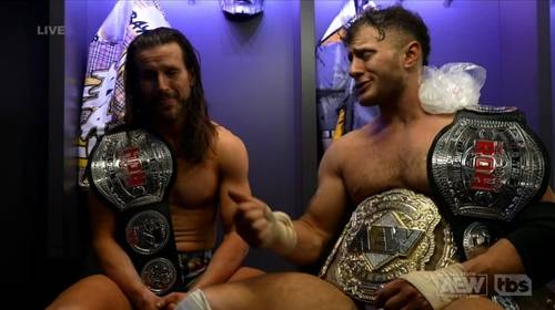 Superluchas - Dos luchadores sentados en un vestuario, agarrando con orgullo sus cinturones de campeonato.
