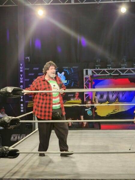Superluchas - Mick Foley, vestido con una camisa a cuadros, de pie en un ring de lucha libre de Ohio Valley Wrestling.